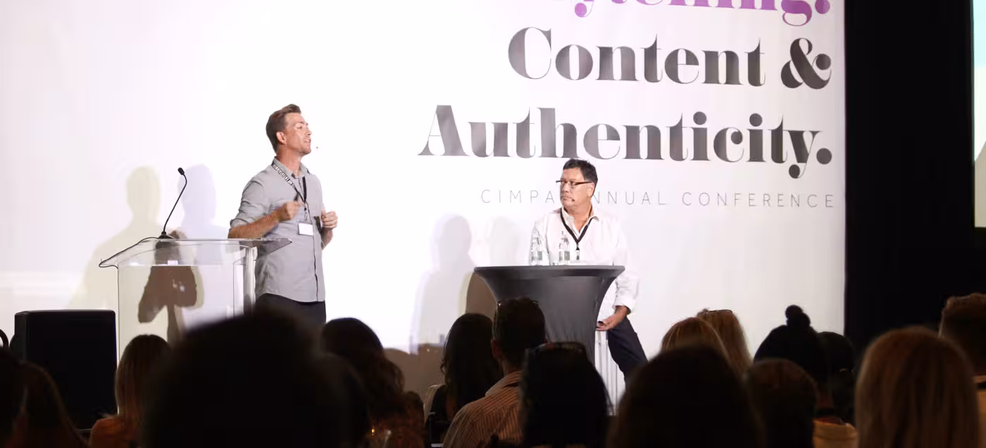 A photo of two speakers on a stage at a conference delivering a presentation.